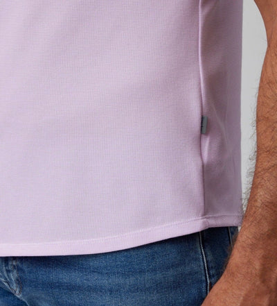 Close-up of a person wearing the Stone Rose SS Pique Shirt 2K7T241 in light purple with textured fabric and blue jeans, showing part of an arm and a small fabric tag on the side seam.