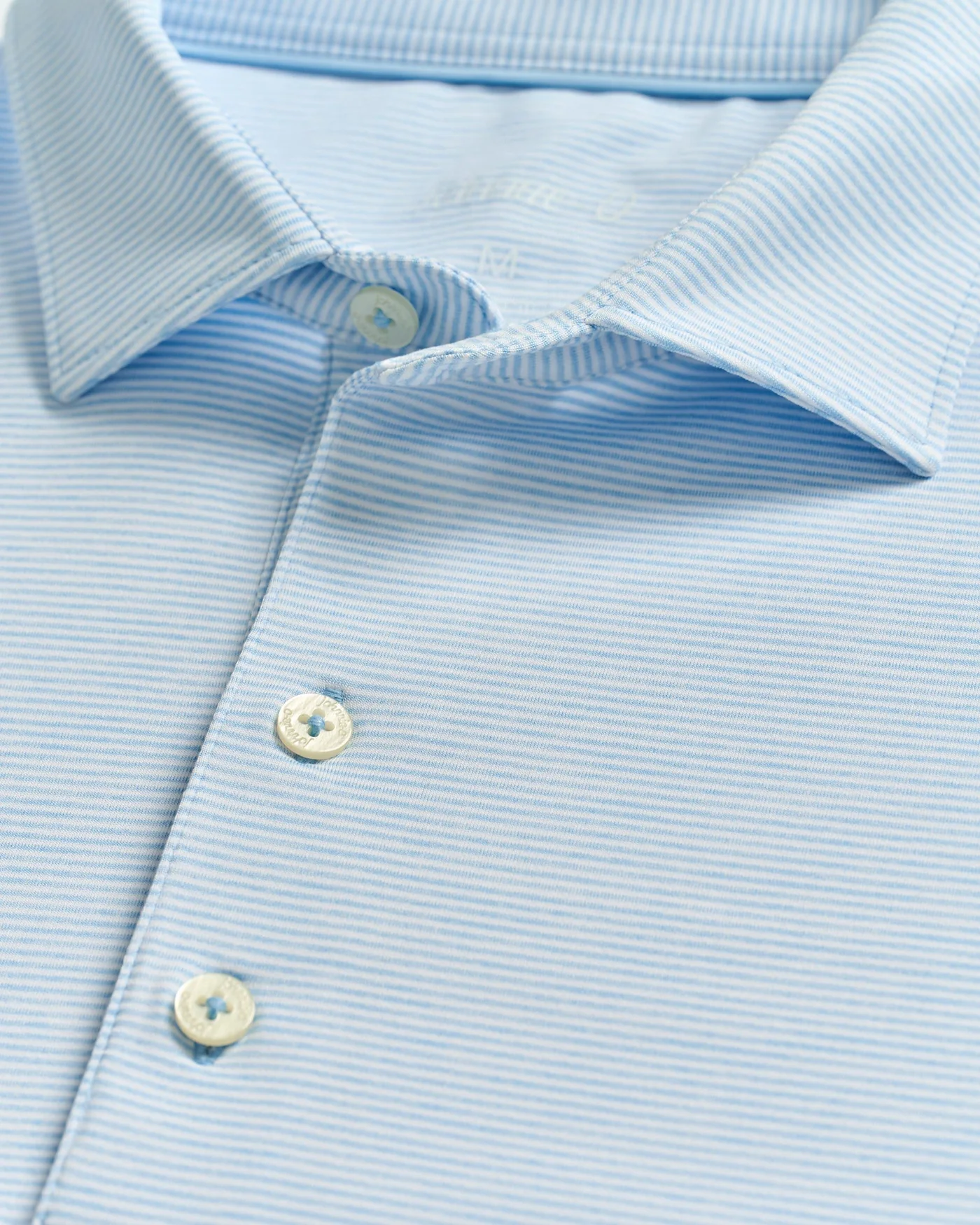 Close-up of the Johnnie-O Lyndonn Stripe Performance Knit Polo by Johnnie-O, featuring light blue thin stripes, white buttons, and a spread collar for a modern twist on the classic style.