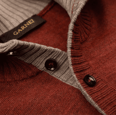 Close-up of the Garnet Sweater 24220, a maroon men's long-sleeve button-up sweater by Garnet, featuring grey inner lining and black buttons. The Garnet brand label is visible at the collar.