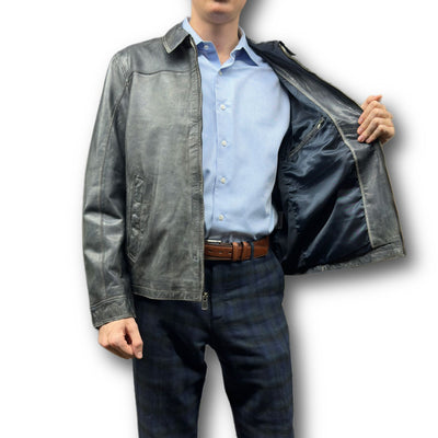 A man in a blue shirt and plaid pants opens the Missani Vintage Leather Jacket 392794, highlighting its inner lining and interior pocket, and showcasing the detailed craftsmanship of this iconic Missani piece.