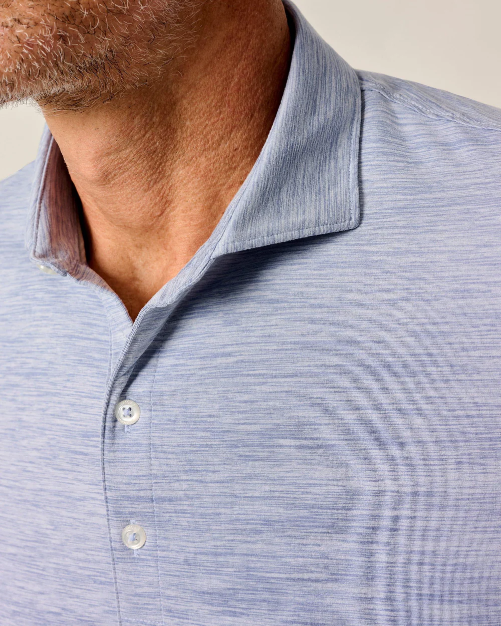 Close-up of a man wearing the Johnnie-O Performance Polo-Huronn, a textured light blue shirt with a button-up collar. Only his neck, chin, and upper chest are visible, emphasizing its lightweight jersey design and UPF 50 sun protection.