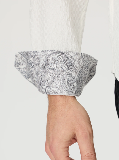 A close-up of a person’s arm wearing the Robert Graham Devonshire Woven Shirt—a white textured, long sleeve button-down featuring an elegant gray paisley pattern on the cuff.