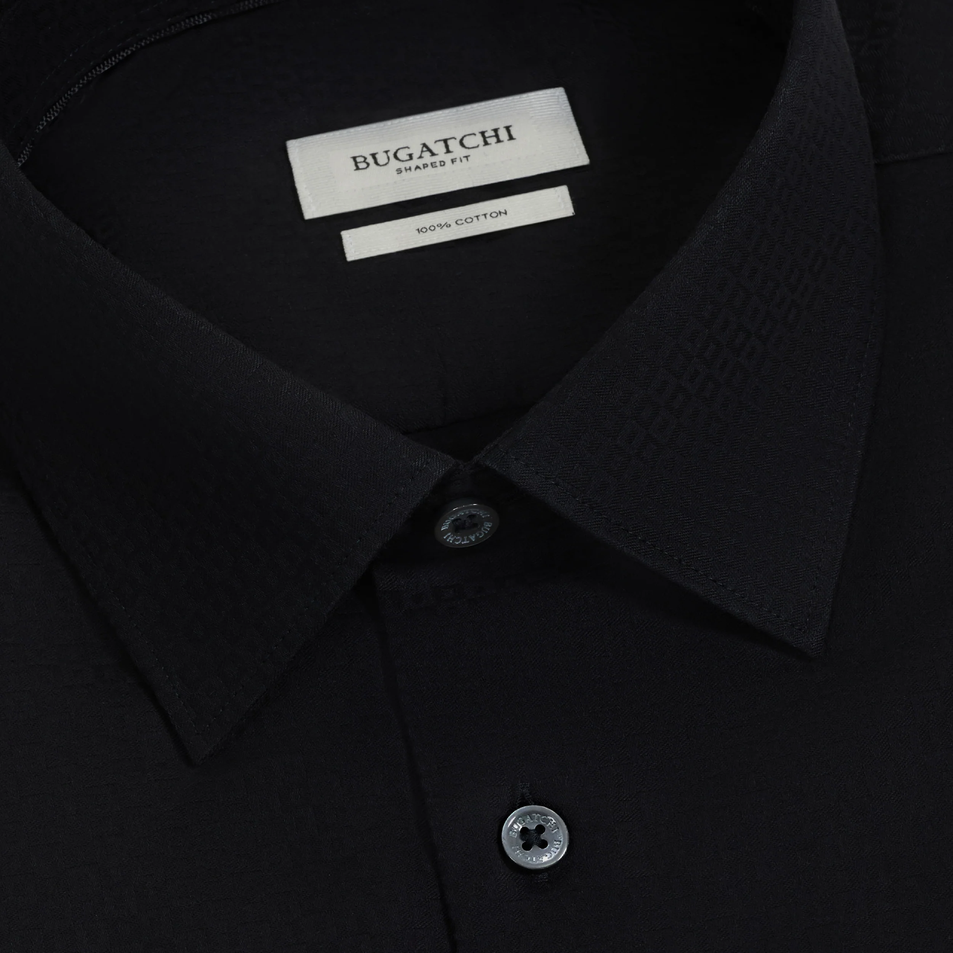 Close-up of a black Bugatchi Julian Tonal Geometric Jacquard Shirt KS4001L3S showcasing a pointed collar, two buttons, and a visible label denoting Shaped Fit and 100% cotton. This wrinkle-resistant men’s dress shirt by Bugatchi combines modern style and comfort in an updated silhouette.