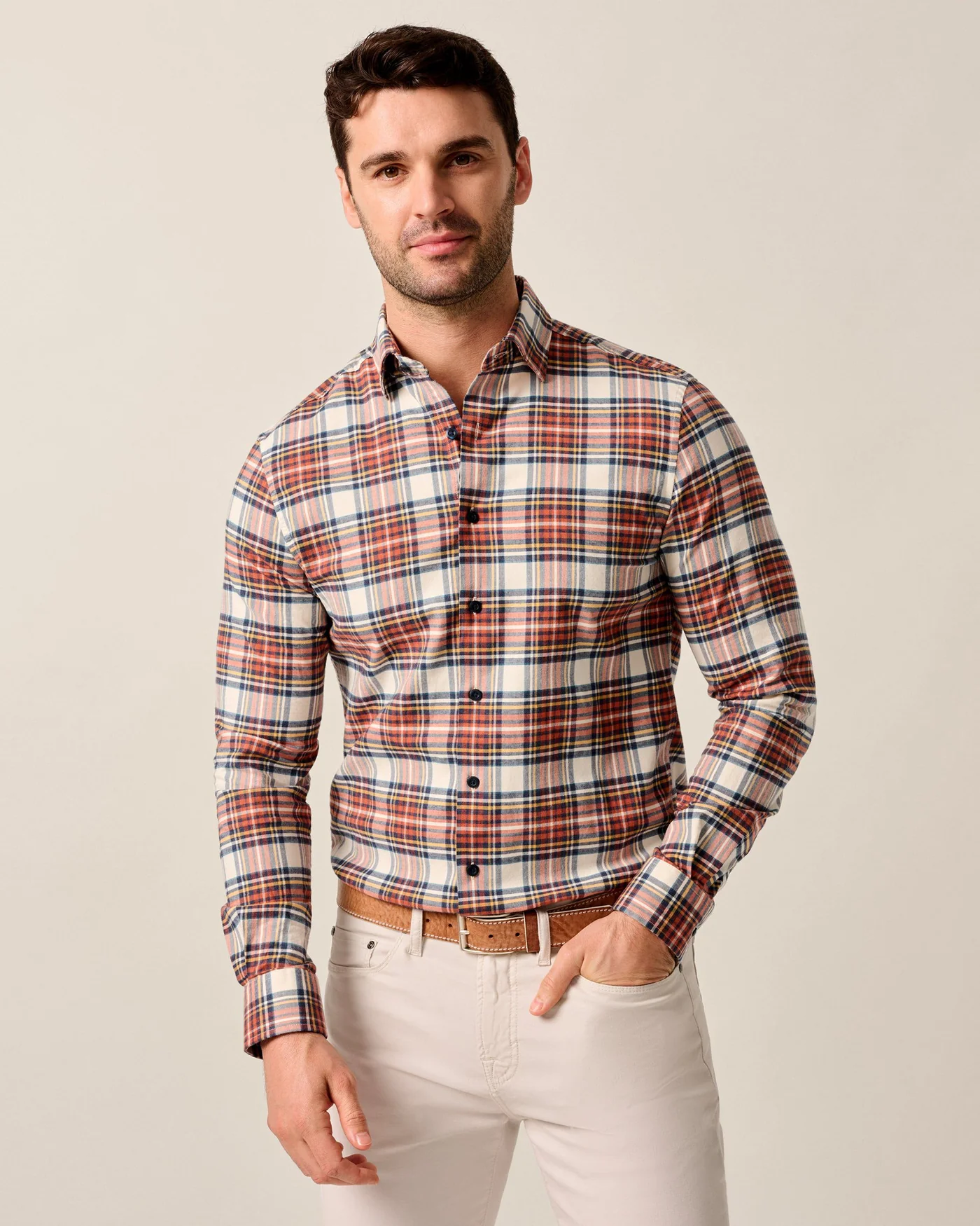 A man stands against a plain light background wearing the Johnnie-O Knick Flannel Plaid Shirt Big & Tall in red, blue, and white plaid by Johnnie-O, paired with beige pants and a brown belt.