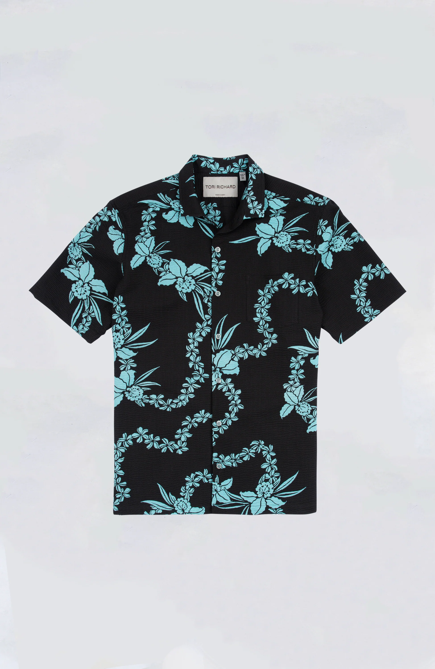 The Tori Richard Lei Hawaiian Shirt by Tori Richard is a black cotton lawn short-sleeve button-up with a light blue floral and vine design, cutaway collar, and is shown laid flat on a plain background.