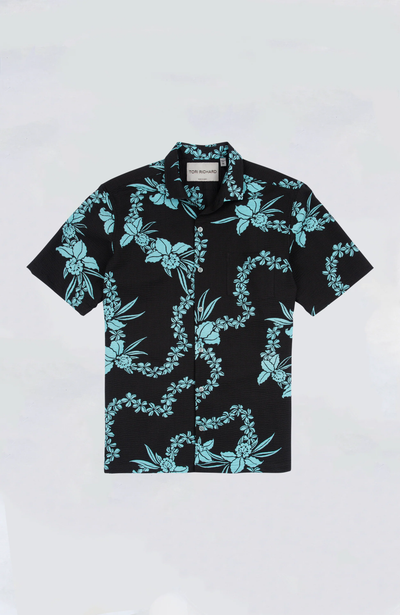 The Tori Richard Lei Hawaiian Shirt by Tori Richard is a black cotton lawn short-sleeve button-up with a light blue floral and vine design, cutaway collar, and is shown laid flat on a plain background.