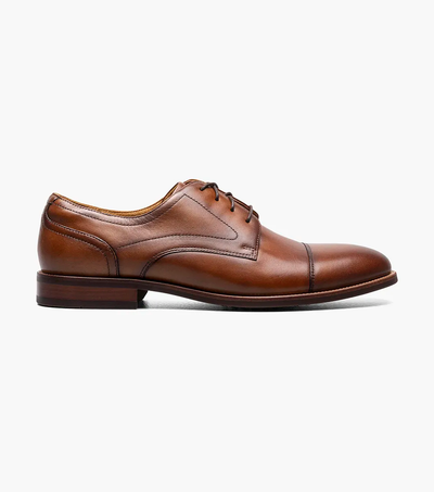 The Florsheim Rucci Plain Toe Oxford, a brown leather men's dress shoe with laces and a low heel, by Florsheim, is shown in profile against a plain white background.