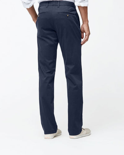 A man wearing Tommy Bahama Boracay Pant Big & Tall in navy blue, a white long-sleeve shirt, and beige slip-on shoes is shown from the back against a plain white background.