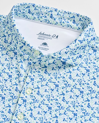 Close-up of the Johnnie-O Charmer Jersey Polo featuring a blue and green floral pattern, white buttons, and a Johnnie-O Performance Medium label inside the collar.