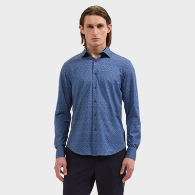 A man stands against a plain background, facing forward with a neutral expression, wearing the Bugatchi James Geometric Sport Shirt KF9188K60—a blue long-sleeve wrinkle-resistant shirt by Bugatchi—and black pants.