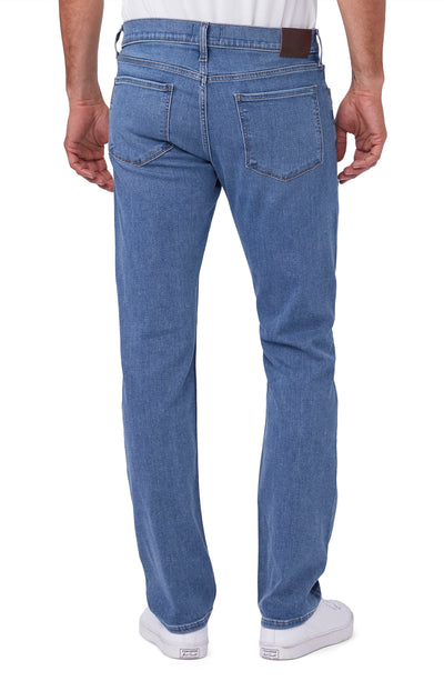 A man wearing Paige Federal Straight Slim Jeans by Paige in medium wash and white sneakers, shown from the back against a white background.