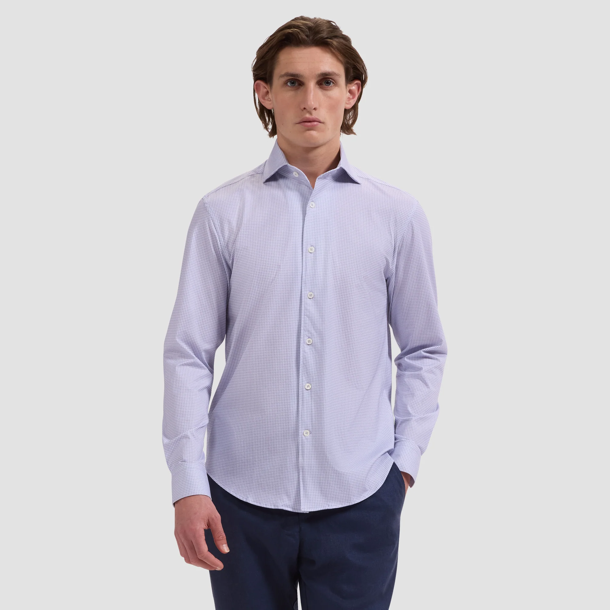 A person wears the Bugatchi OP Devon OoohCotton® Geometric Shirt JF9507K80, a light blue, wrinkle-resistant shirt from Bugatchi, and dark pants while standing against a plain light gray background.