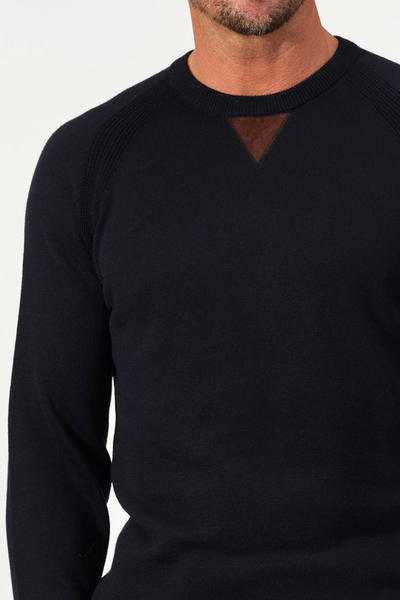 A man wears a black Garnet Milano Crew Sweater 2522003CS, a long-sleeve crew neck featuring a brown triangular patch at the collar.
