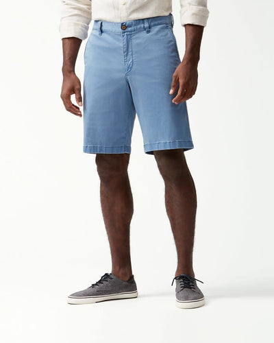 A person wearing a white long-sleeve shirt, Tommy Bahama Boracay Shorts Big & Tall in light blue, and gray sneakers stands against a plain white background.