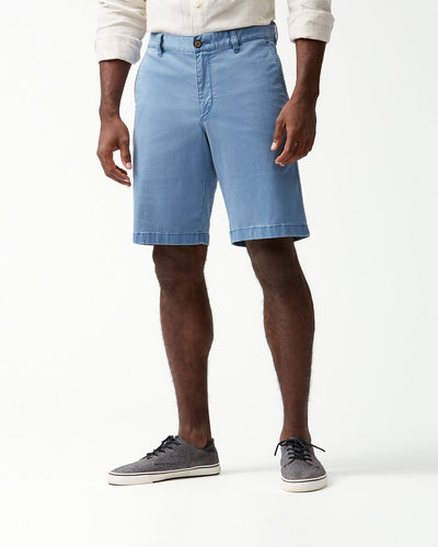 A man models Tommy Bahama Boracay Shorts Big & Tall in light blue with a white long-sleeve shirt and gray sneakers, standing against a plain white background.