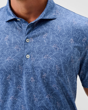 Close-up of a person wearing the Johnnie-O Osmond Big & Tall Polo by Johnnie-O, featuring a blue pattern with leaf and flamingo design, short sleeves, moisture-wicking fabric, UPF 50 protection, shown from upper torso to collar.