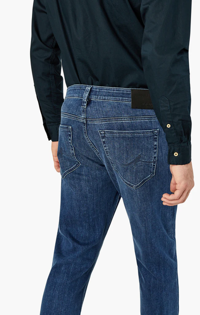 A person is shown from the back with one hand by their side, wearing a dark long-sleeve shirt and 34 Heritage Charisma Mid Urban relaxed fit, straight leg jeans in premium stretch denim by 34 Heritage.