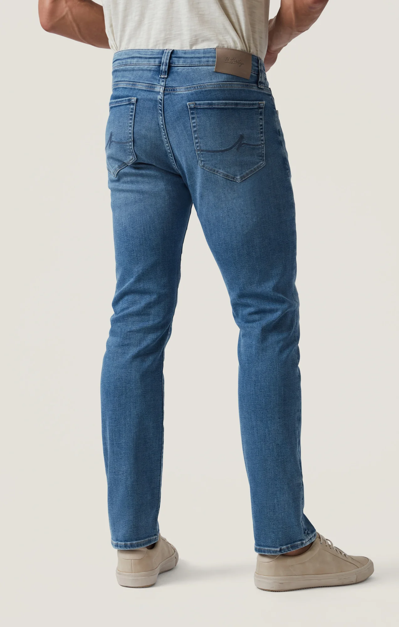 A person is shown from the back, standing against a plain light background, wearing the 34 Heritage Courage Jeans Organic Ultra in light blue and beige sneakers.