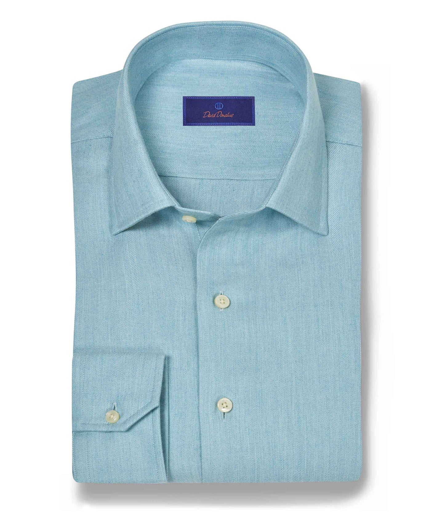 The David Donahue Herringbone Sport Shirt CBSM10100 is a light blue Pima cotton shirt with a herringbone weave, spread collar, cream buttons, and adjustable cuffs, shown neatly folded on a white background.