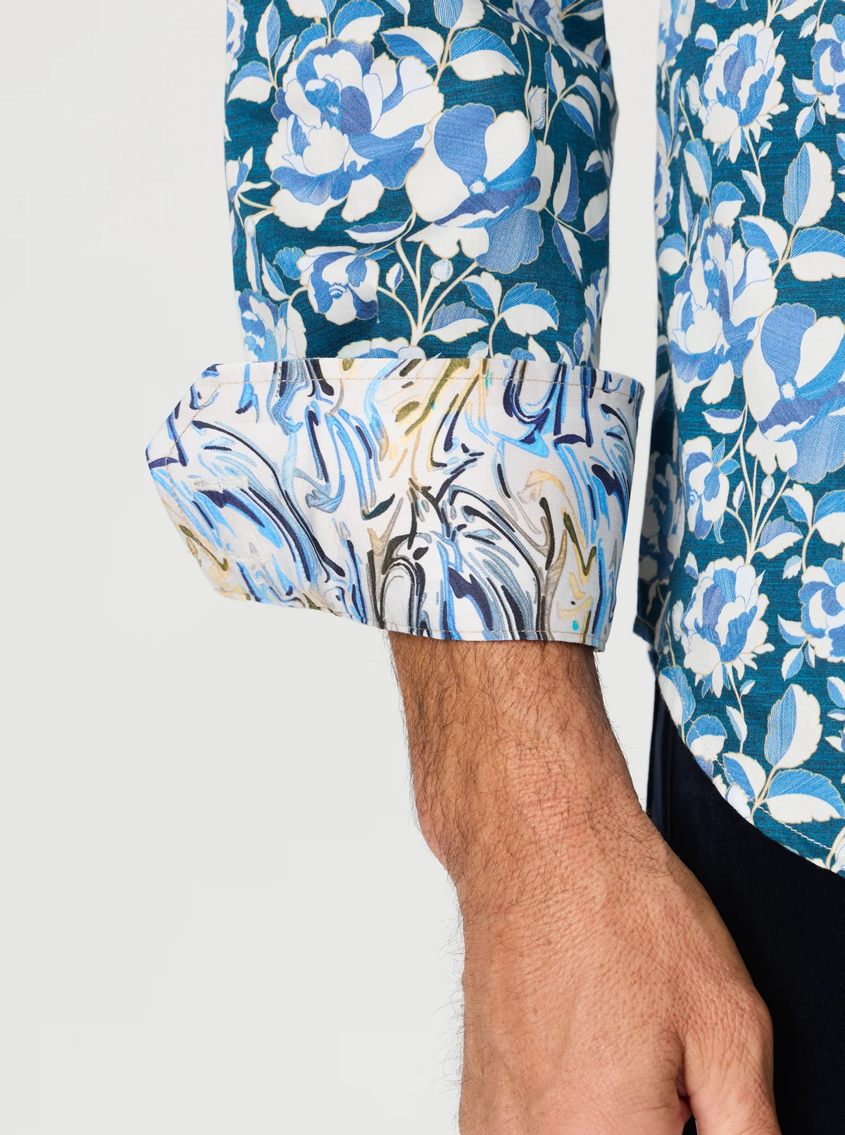 A person wears the Robert Graham Euclid Long Sleeve Shirt Big & Tall, featuring blue floral fabric and turned-up cuffs that reveal a contrasting marble-patterned inner lining.