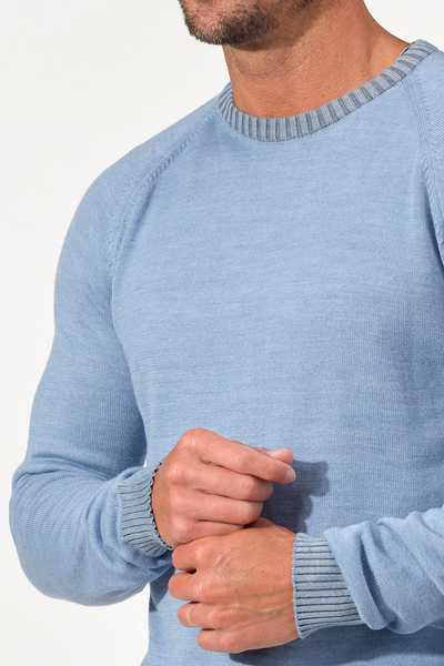 A man models the Garnet Crew Valmont Sweater 2522001CS by Garnet—a light blue men's Merino wool knit with gray ribbed collar and cuffs—shown from shoulders to waist against a plain background.