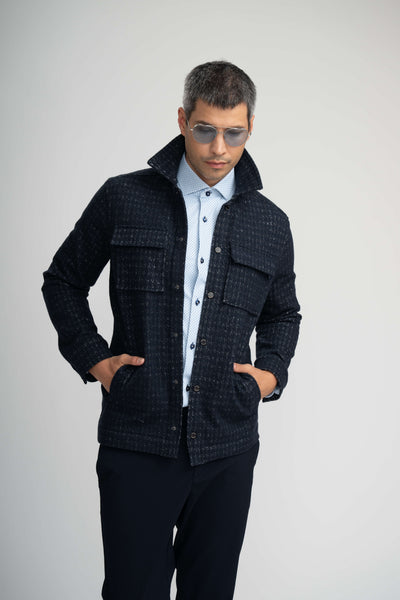 A man wearing a Stone Rose Hunter Knit Houndstooth Jacket over a light-colored patterned button-down shirt and sunglasses, with his hands in his jacket pockets.