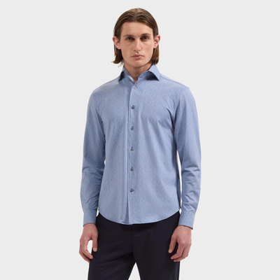 A man wearing a light blue, long-sleeved Bugatchi Devon Foliage Prt Sport Shirt (KF9423K80) and dark pants, standing against a plain white background.
