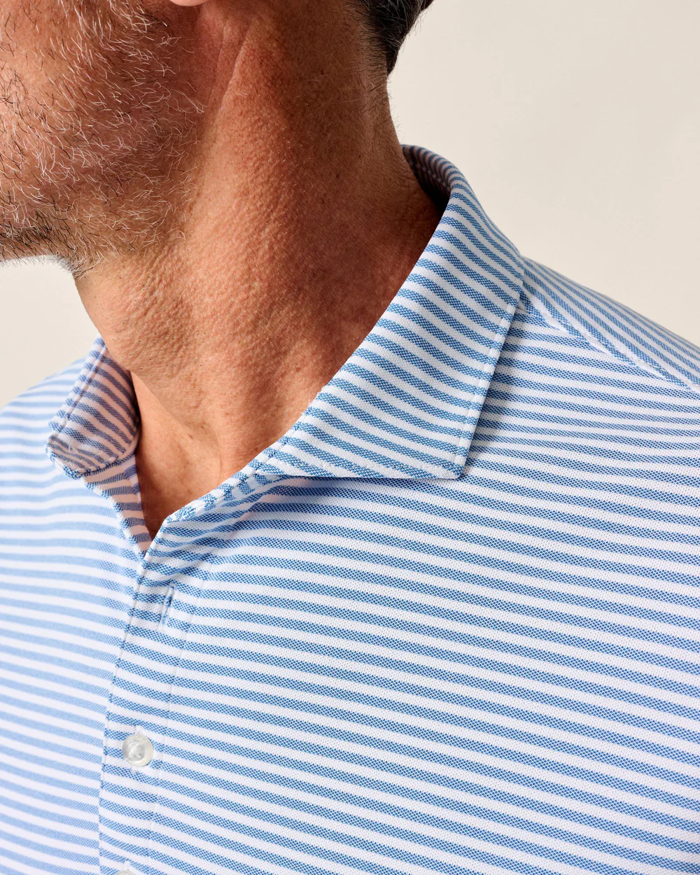 Close-up of a man’s neck and shoulder wearing the Johnnie-O Performance Polo- Stetsons, a light blue and white striped golf shirt by Johnnie-O, with his face partially out of frame.