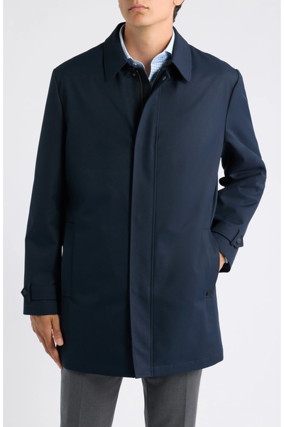Man wearing a navy blue Hart Schaffner Marx Milo Waterproof All-Weather Jacket over a light blue checked shirt and grey trousers.