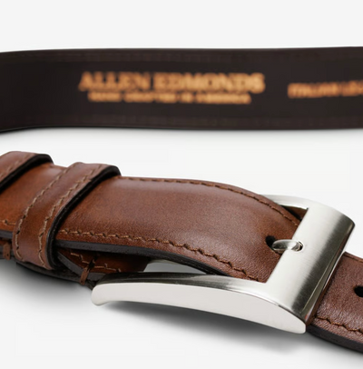 The Allen Edmonds Wide Basic Belt, featuring brown premium Italian calfskin leather and a silver buckle, rests on a white surface. Handcrafted in America, the inside of the belt bears the gold Allen Edmonds logo.