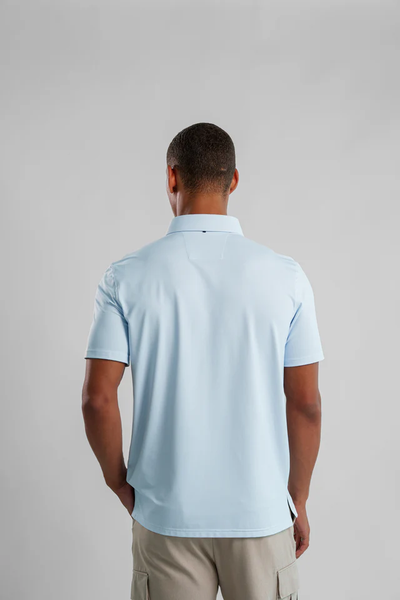 A man faces away from the camera, wearing a light blue Stone Rose Apex Birdseye Polo BSCSSP51 and light shorts against a gray backdrop—an ideal modern classic for your summer wardrobe.