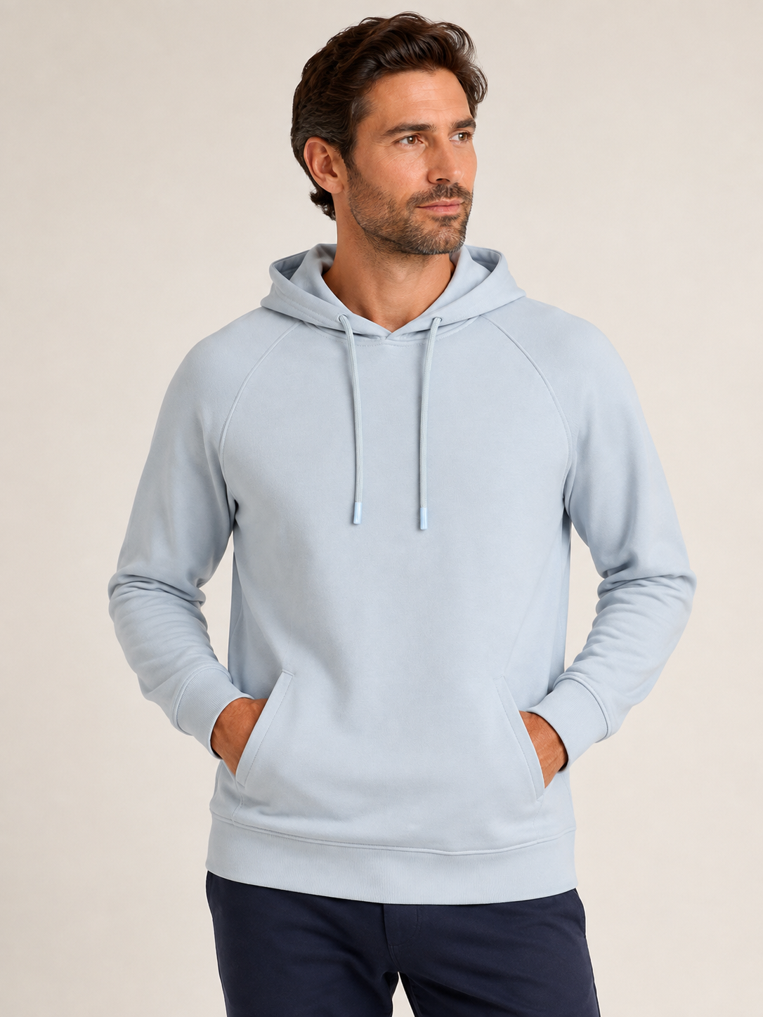 A man stands facing slightly left against a plain beige background, wearing the Georg Roth Scuba Hoodie Big & Tall in light blue by Georg Roth, featuring front pockets, paired with dark pants.