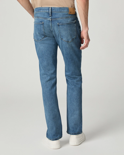 A person is shown from the back wearing Paige Federal Straight Slim Jeans in a medium wash with white sneakers, set against a plain background.