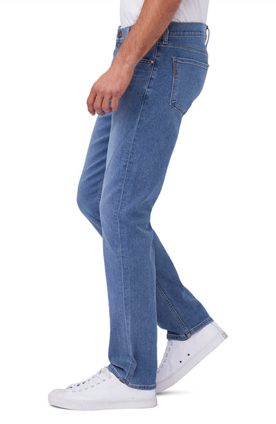 A person in Paige Federal Straight Slim Jeans by Paige, styled with a white shirt and white sneakers, stands in side profile against a white background.