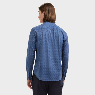 A person with straight, medium-length brown hair is shown from the back, wearing the Bugatchi James Geometric Sport Shirt (style KF9188K60) by Bugatchi—a blue patterned long-sleeve performance shirt—paired with dark pants against a plain white background.