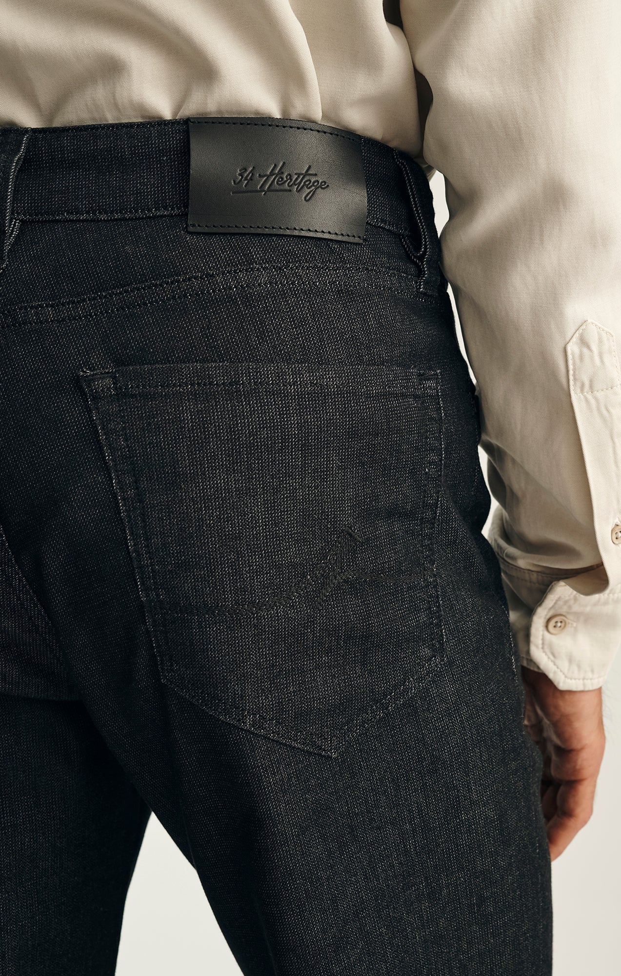 Close-up of a person wearing 34 Heritage Charisma Sporty Big&Tall ultra-stretchy dark twill jeans, featuring a visible 34 Heritage leather patch above the back pocket, paired with a light-colored button-down shirt.