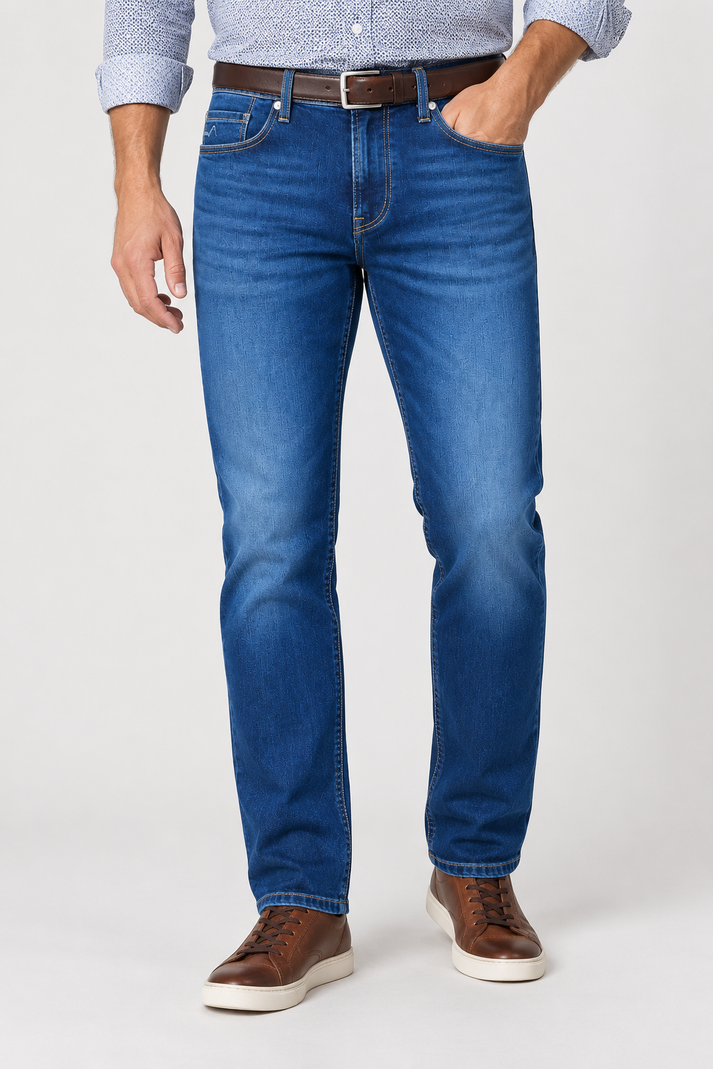 Man wearing Alberto Pipe 1984 Stretch Denim blue jeans, a brown leather belt, a patterned button-down shirt, and brown leather sneakers.