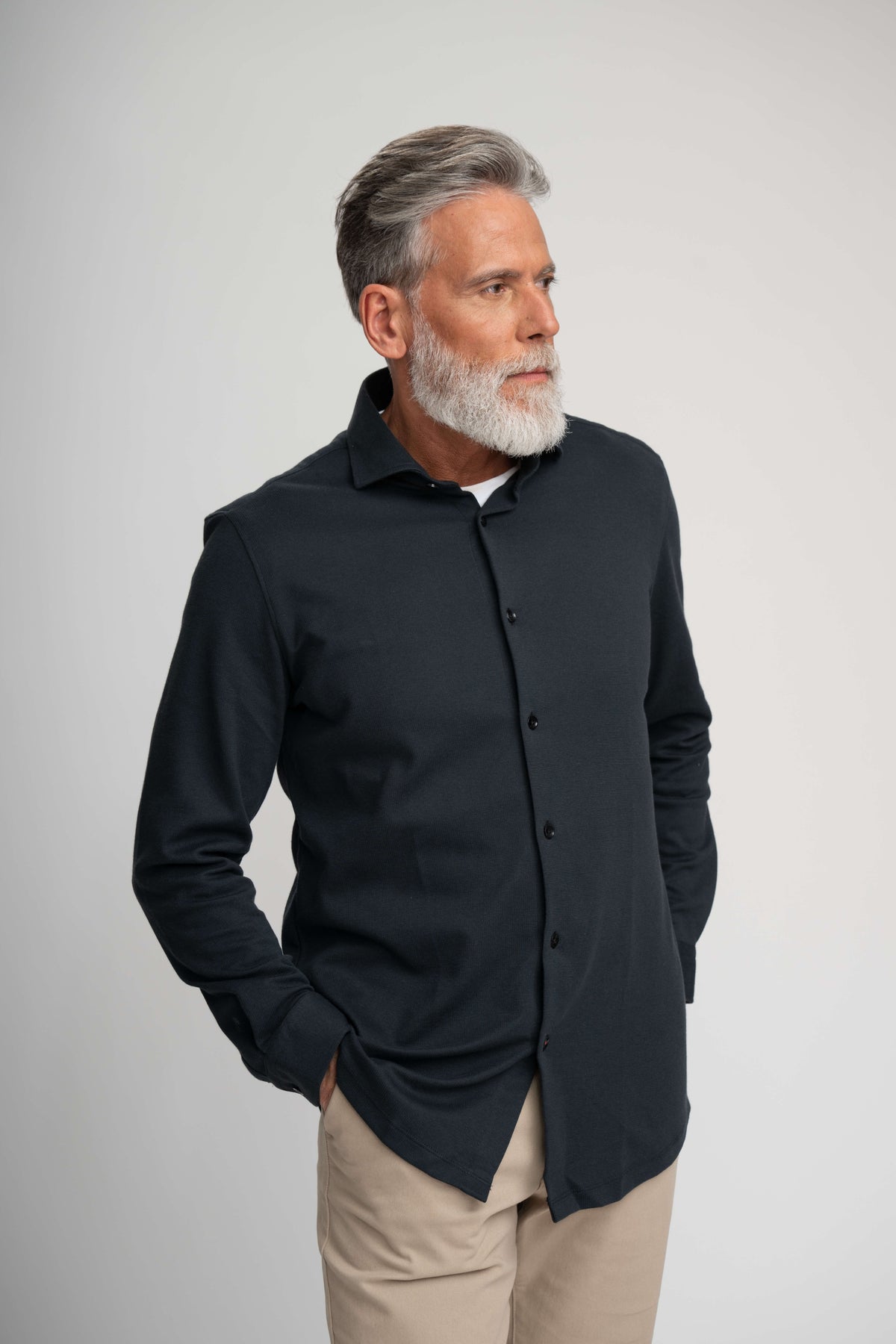 A man with a grey beard wearing a navy blue Stone Rose ORIGIN - Long Sleeve Tech Pique Shirt and tan pants.