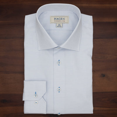 A neatly folded light blue dress shirt with a subtle micro dot jacquard pattern, buttoned up and placed on a dark wooden surface. The label reads Hagen. This Hagen Micro Dot Shirt MB7940100 is crafted from 100% cotton for exceptional comfort and exemplifies modern fit menswear.