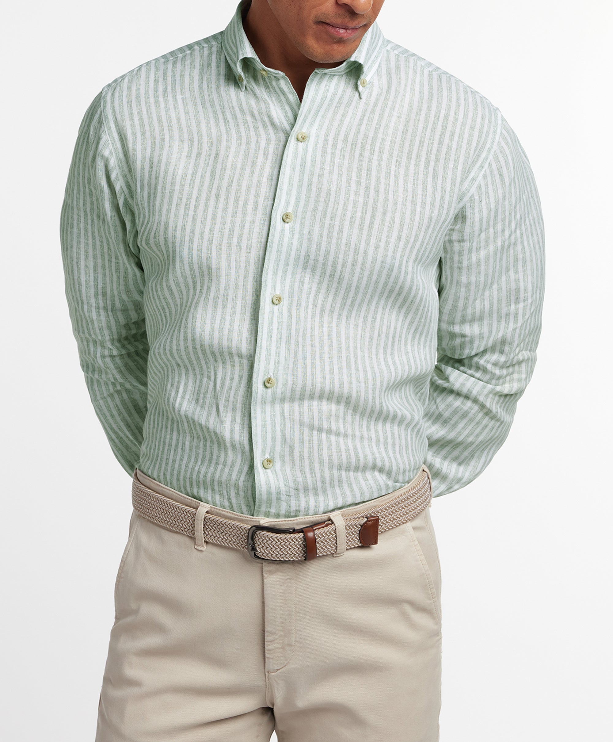 A man stands with hands behind his back, wearing a David Donahue Linen Stripe Sport Shirt in sage and white, paired with a beige braided belt and light khaki pants.
