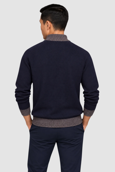 A man, seen from behind against a plain light gray background, is wearing the Garnet Tate Contrast-Trim Mock Neck Sweater 2622022 by Garnet—featuring a navy blue body with gray ribbed collar, cuffs, and hem—paired with dark pants.