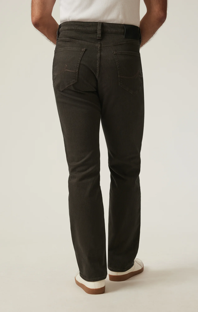 A person is shown from the back against a neutral background wearing 34 Heritage Charisma Diagonal Big&Tall dark brown ultra-stretchy jeans, a white shirt, and white shoes.