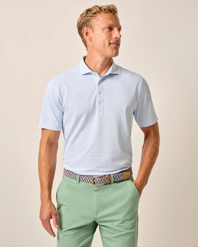 A man wearing the Johnnie-O Performance Polo-Stetsons by Johnnie-O in light blue stripes, mint green pants, and a patterned belt stands against a plain background.
