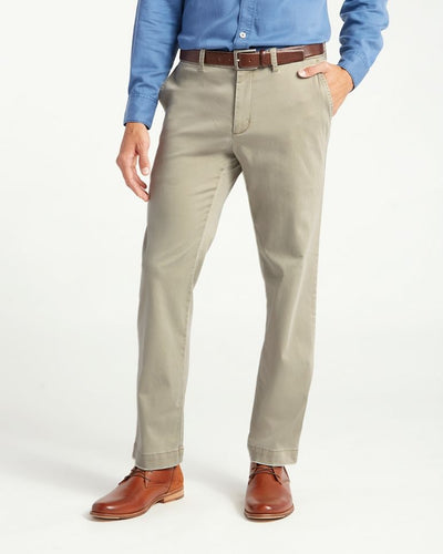 A person wearing Tommy Bahama Boracay Pant Big & Tall chinos, a blue button-up shirt, a brown belt, and brown leather shoes stands with one hand in their pocket against a plain background.