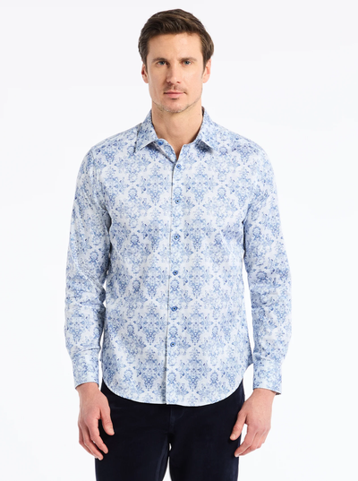 A man stands facing forward wearing the Robert Graham Delancey Woven L/S Shirt B&T, a light blue and white floral allover print men’s cotton shirt from Robert Graham, paired with dark pants against a plain, light background.
