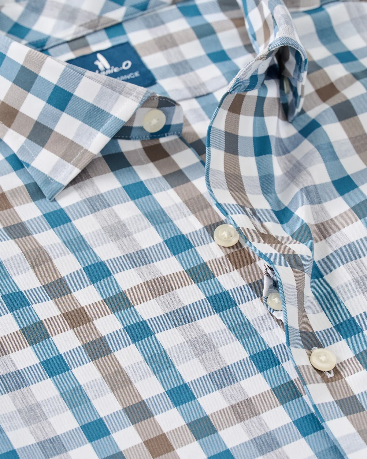 Close-up of the Johnnie-O Cay Exploded Gingham Shirt Big & Tall by Johnnie-O, showcasing a blue, brown, and white plaid pattern with white buttons and a structured collar. This moisture-wicking performance shirt combines comfort and style for all-day wear.