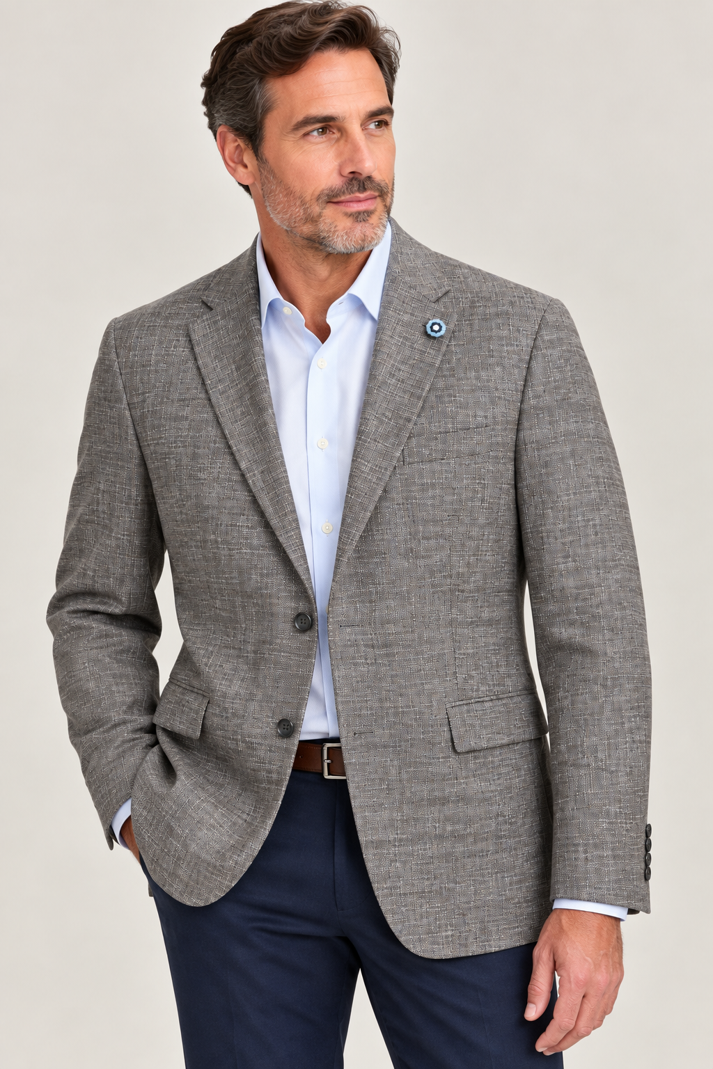 A man wearing the Hart Schaffner Marx Grey and Brown New York Sport Coat 3900010 over a white dress shirt and navy pants stands with one hand in his pocket, looking to the side.