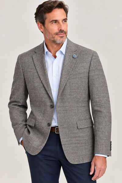 A man wearing the Hart Schaffner Marx Grey and Brown New York Sport Coat 3900010 over a white dress shirt and navy pants stands with one hand in his pocket, looking to the side.
