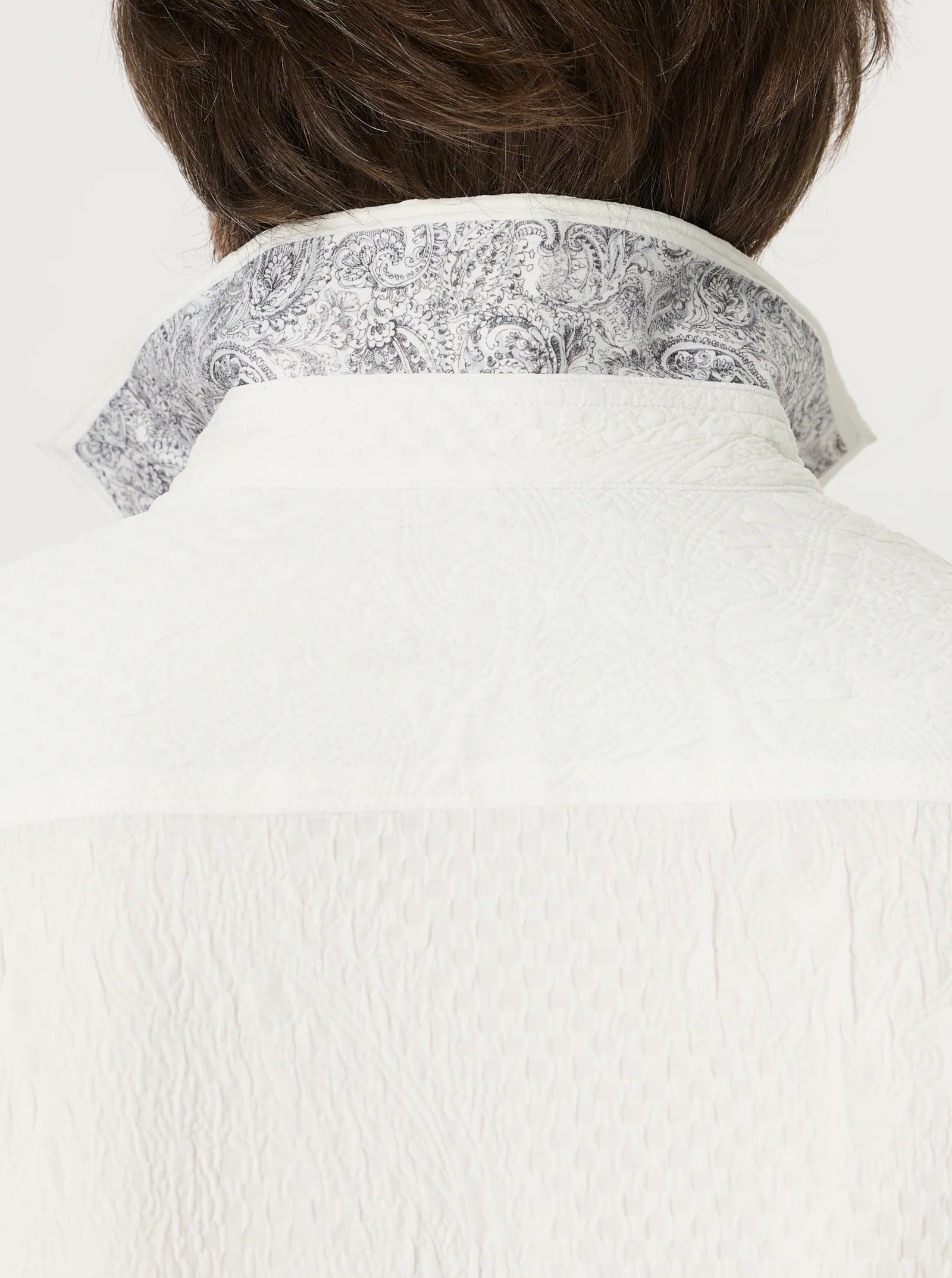 Close-up of the back of a person wearing the Robert Graham Devonshire Woven Shirt, a white long-sleeve style with the collar turned up to reveal a gray and white floral paisley jacquard pattern on the inside—a signature detail from Robert Graham.