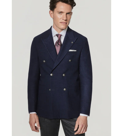 A man wearing the Jack Victor Hampton SC C1273 tailored-fit navy double-breasted sport coat, crafted from 100% wool by Jack Victor, paired with a lavender dress shirt, pink tie, and gray trousers, stands against a plain light background.